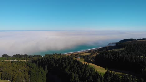 Approaching-an-ocean-of-clouds-at-the-coastline,-with-green-farmland-in-the-foreground