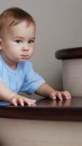 little smart baby in blue romper plays nearby the stairs. adorable healthy caucasian child indoors being active. vertical video