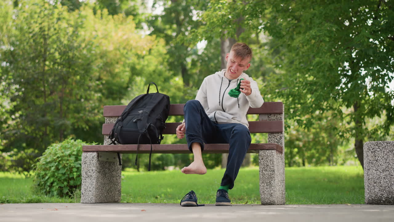 Man resting outside, Student relaxing beneath leafy trees, Man enjoying peaceful moment outdoors under green canopy, Individual taking break outdoors surrounded by lush green foliage