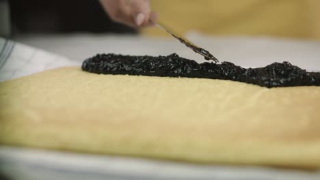 close up of berry jam being put on a swiss roll cake dough by a vegan chef