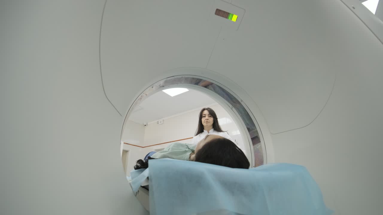 женщина-пациент проходит ct или мрт под наблюдением радиолога в современной медицинской клинике. пациент лежит на постели для ct или мrт, двигаясь внутри машины.