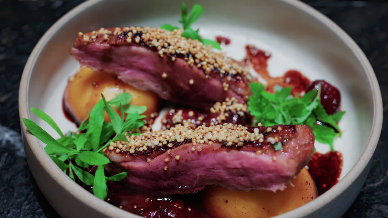 Close up of roasted duck breast plated with caramelized pear, crispy grains, and green herbs