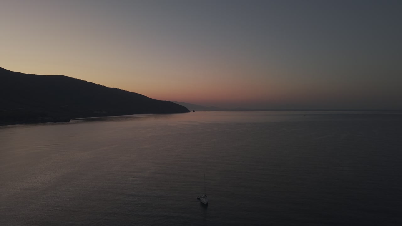 Aerial drone forward shot approaching a sailboat on calm waters at sunrise in the Aegean Sea near Lesbos, Greece.