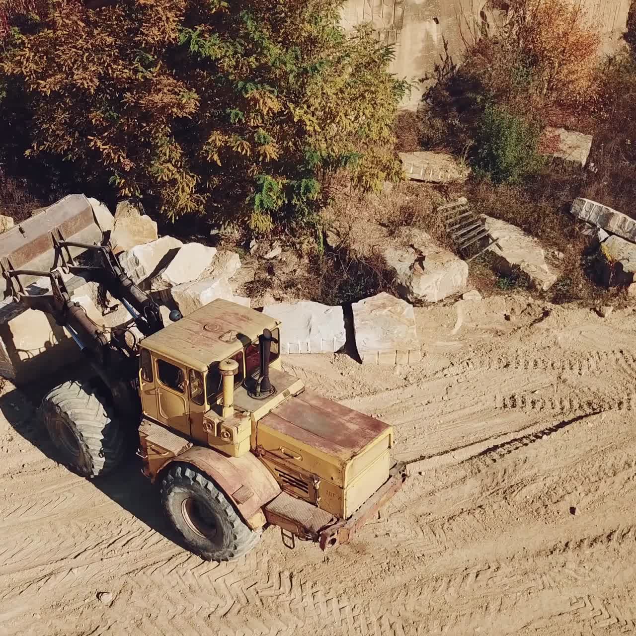 specially equipped machine with a bucket id working near a quarry with stones on the background of sand.