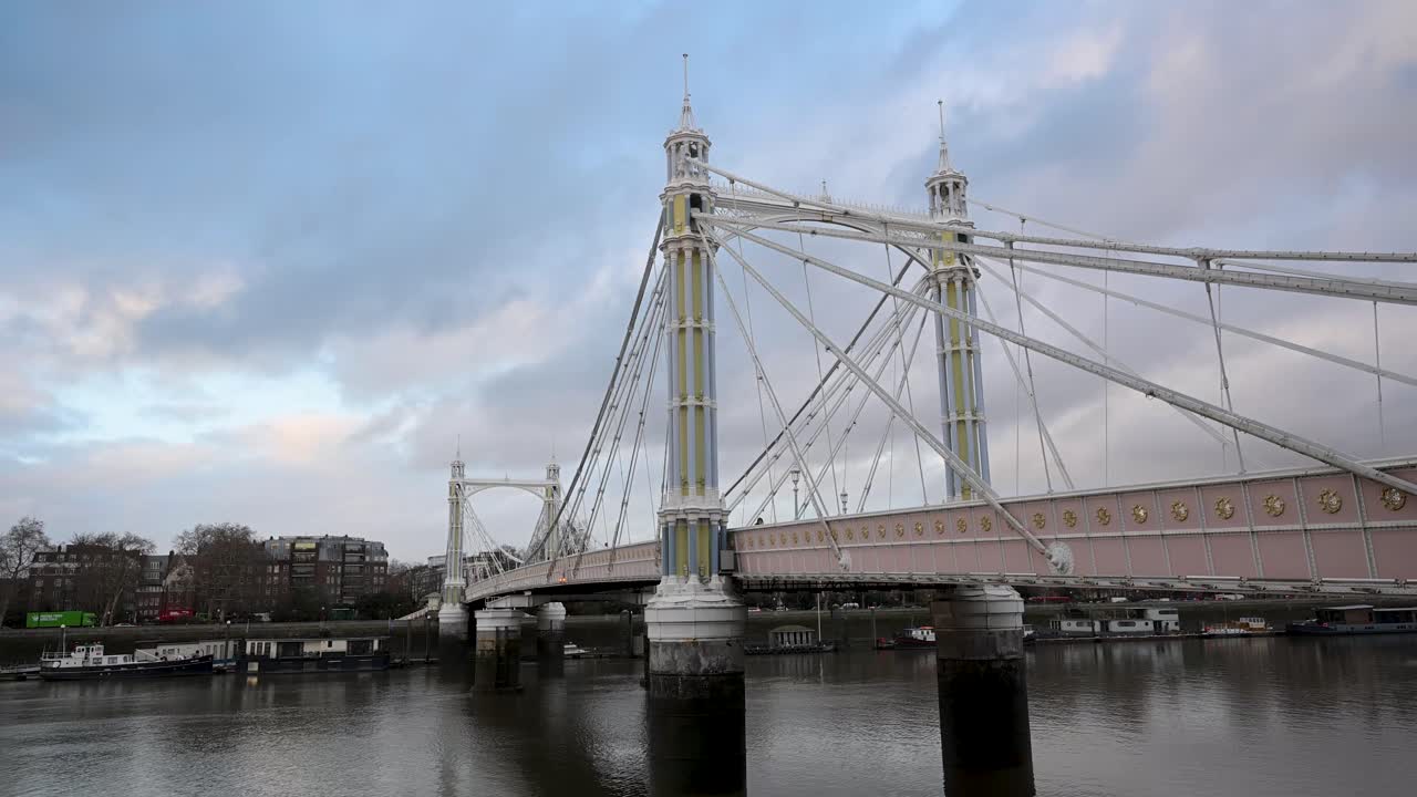Sidevisning av Albert Bridge som spenner over elven, og viser dens utsmykkede fjæringsdesign med tårn og kabler som lyser mykt om kvelden