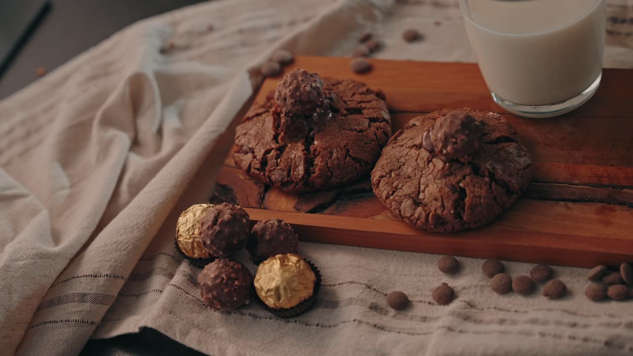 Biscotti al cioccolato su un tagliere di legno con caramelle e un bicchiere di latte, al chiuso