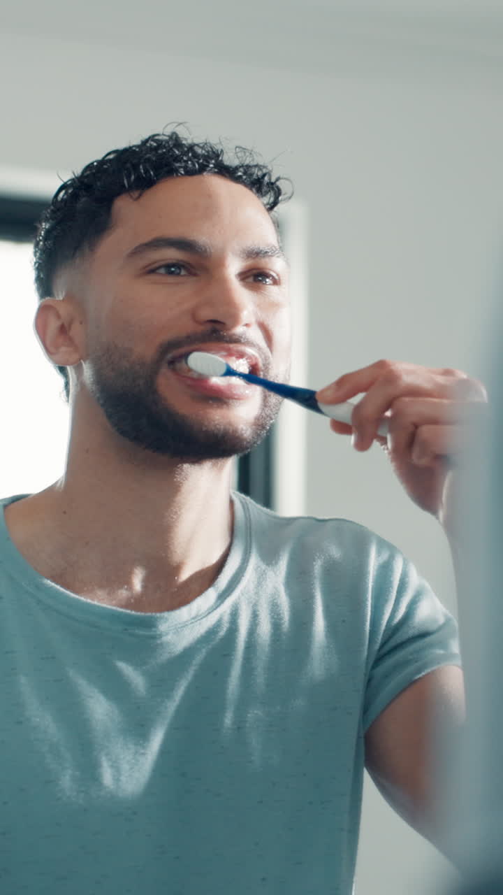 Young Man Brushing Teeth in Bathroom Mirror
