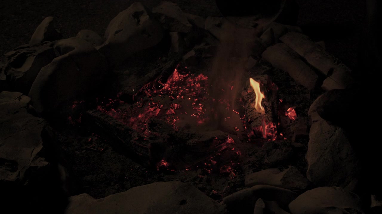 Slow motion of campfire in stone fire pit being put out with sand and bucket