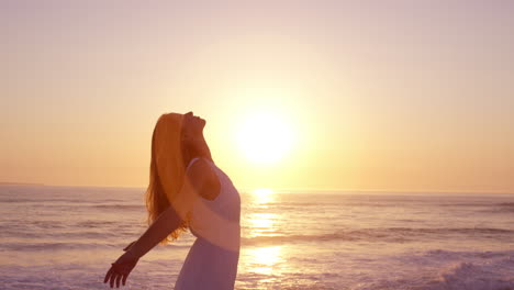 Mujer-Feliz-Libre-Con-Los-Brazos-Extendidos-Disfrutando-De-La-Naturaleza-En-La-Playa-Al-Atardecer-Con-La-Cara-Levantada-Hacia-El-Cielo-En-Cámara-Lenta-Dragón-Rojo