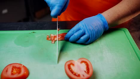 Cook-in-gloves-cutting-tomatoes-on-a-cutting-board,-close-up