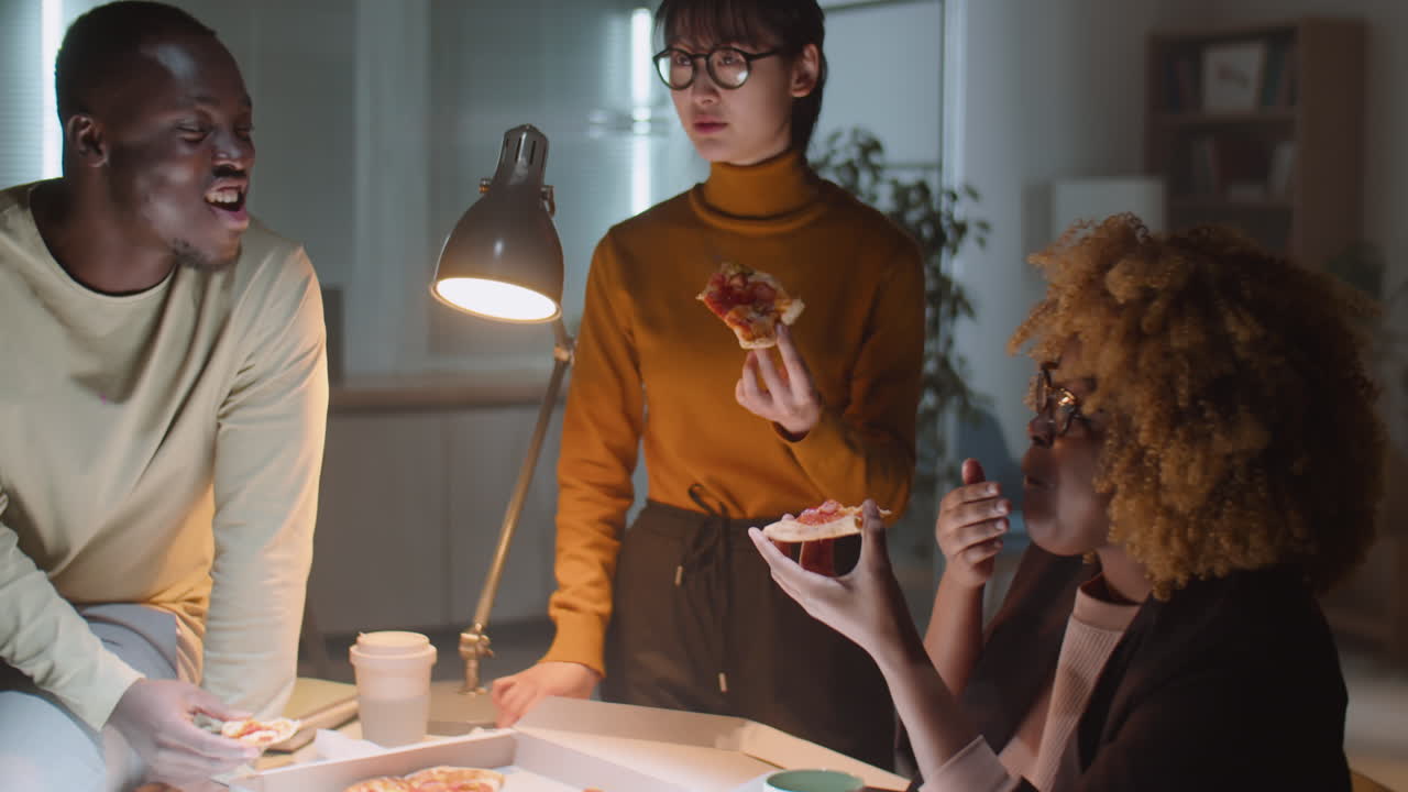 Multiethnic Business Team Eating Pizza in Office at Night