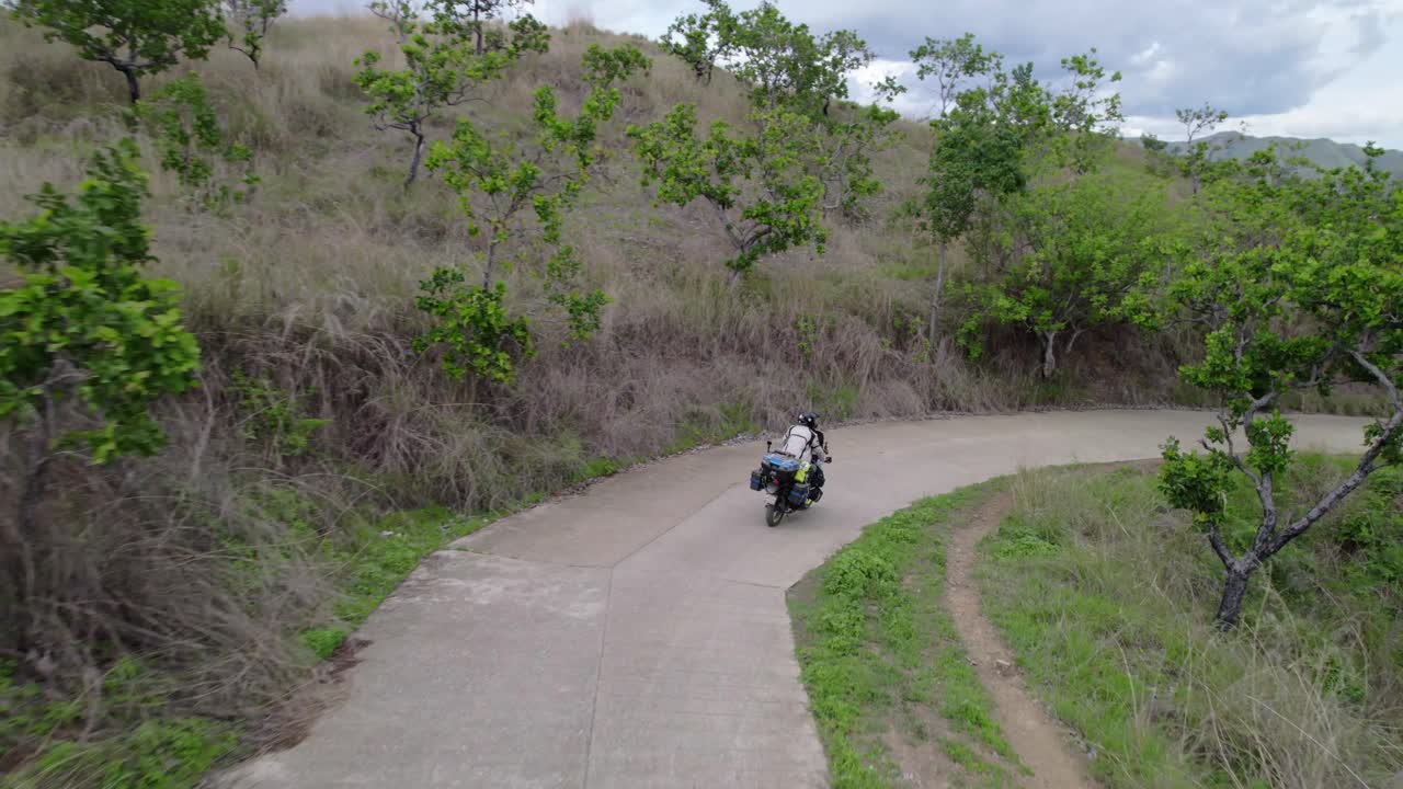 Un motorista solitario se embarca en un viaje en moto por un camino de tierra remoto y sinuoso, donde la carretera abierta le espera.