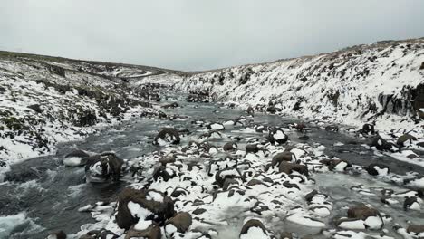Verschneite-Felsen-Auf-Fließendem-Fluss-Im-Isländischen-Winter,-Schöne-Landschaft,-Luftaufnahmen