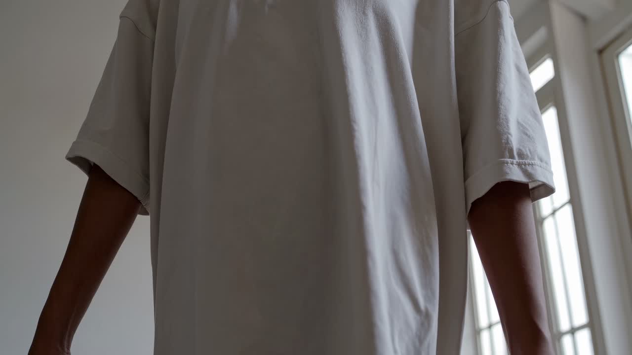 Low-angle shot of a person in a loose white shirt, arms relaxed