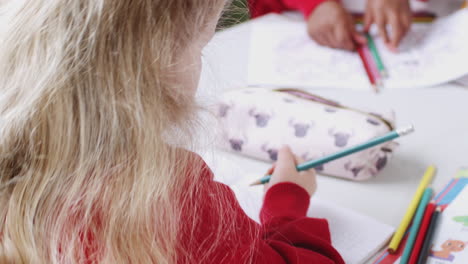 Caucasian-schoolgirl-drawing-at-desk-in-an-infant-school-classroom,-close-up,-over-shoulder-view