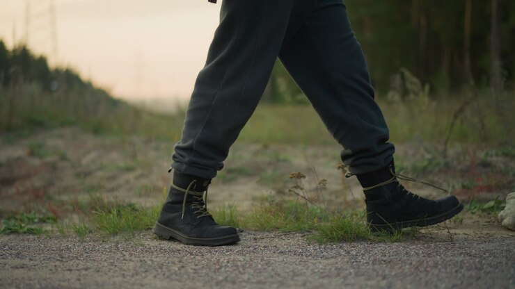 closeup caucasian hiker boots walking gravel dusk, steady stride across rural roadside, rugged laces and textured soles, soft golden hour light, distant pine silhouette, mood of perseverance and focus
