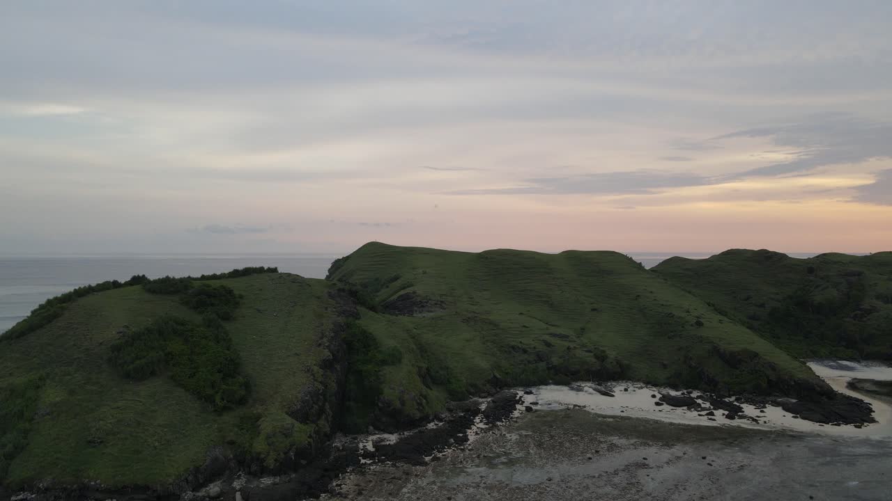 Pemandangan Udara Perbukitan Hijau dan Garis Pantai Berbatu Saat Senja