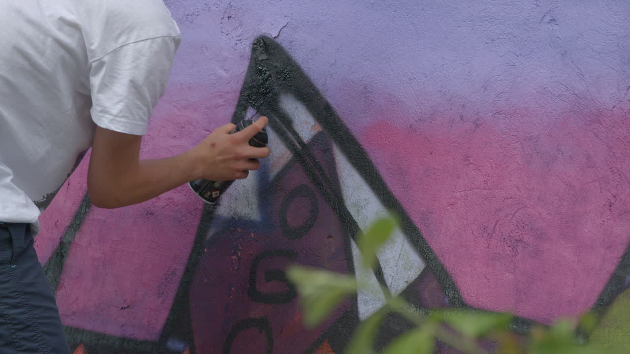 Unrecognizable man doing spray paint graffiti on a wall in slow motion. Vandalism.