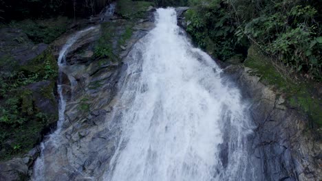 Drone-near-a-waterfall,-moving-up-revealing-it