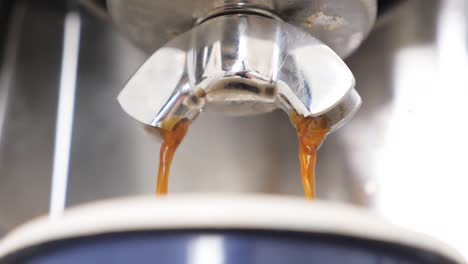 Slow-motion-close-up-of-beautiful-rich-brown-espresso-pouring-out-of-a-stainless-steel-espresso-maker-into-a-blue-mug