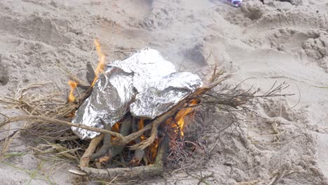 fish wrapped in foil cooking on a fire on the beach