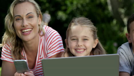 porträt einer süßen familie, die auf dem gras liegt und elektronische geräte benutzt