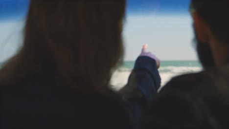 vista trasera de una mujer apuntando con el dedo mostrando las olas del mar al hombre en el coche 4k