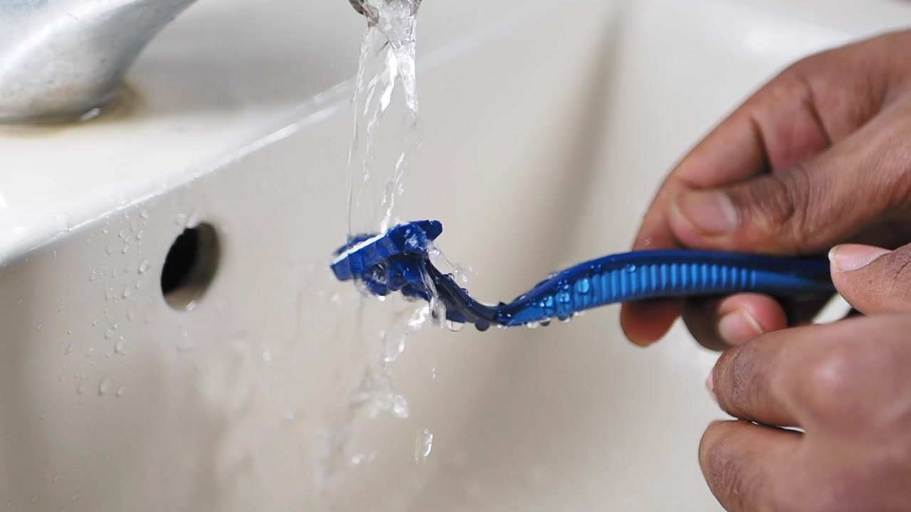 Person Rinsing a Disposable Razor Under Running Water