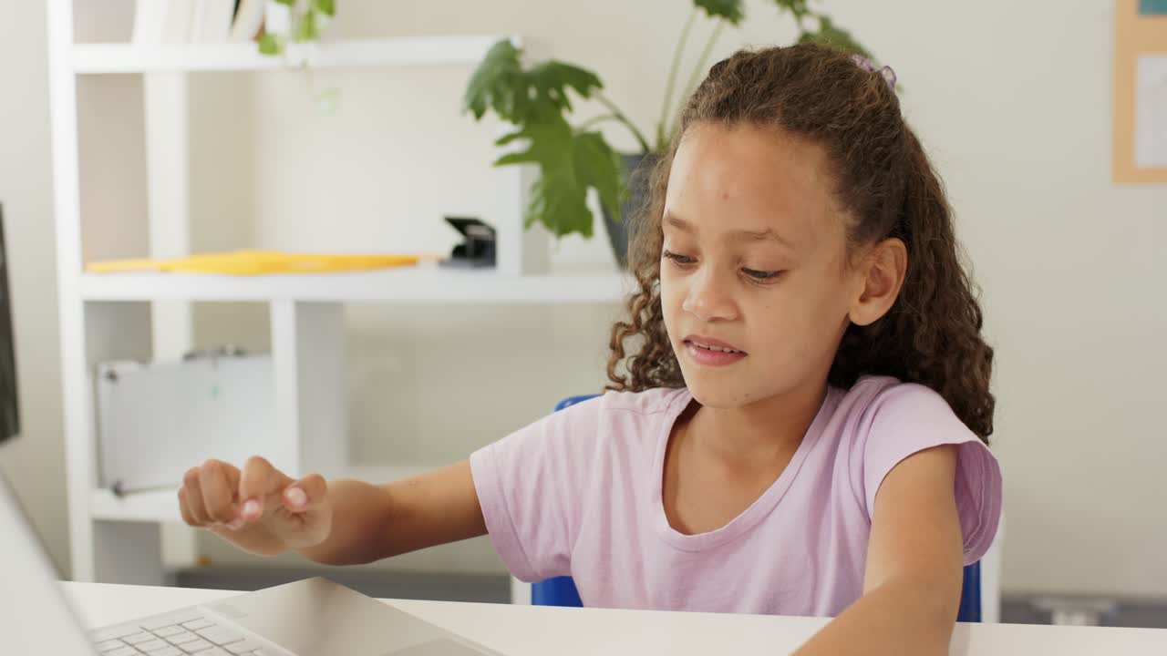 Bambino afroamericano che appoggia le mani sul laptop, digitando usando il touchpad a una scrivania bianca mentre fa i compiti.