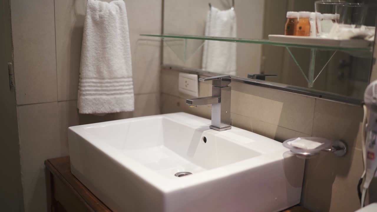 Elegant four star hotel bathroom featuring a sleek white sink, towel, and glass shelf with amenities, creating a welcoming and clean atmosphere for guests