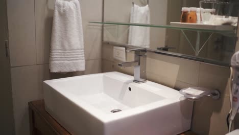 elegant four star hotel bathroom featuring a sleek white sink, towel, and glass shelf with amenities, creating a welcoming and clean atmosphere for guests