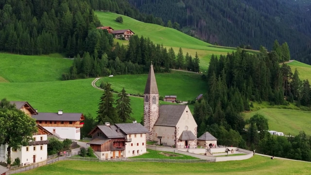 Spokojny letni widok kościoła Santa Maddalena – malownicze zielone wzgórza, przytulne domy.