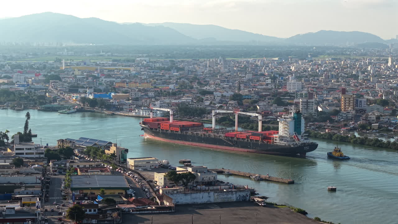 Bird's eye aerial shot of a huge industrial transportation cargo ship entering Itajaí port, Itajaí-Acu river, Santa Catarina, Brazil