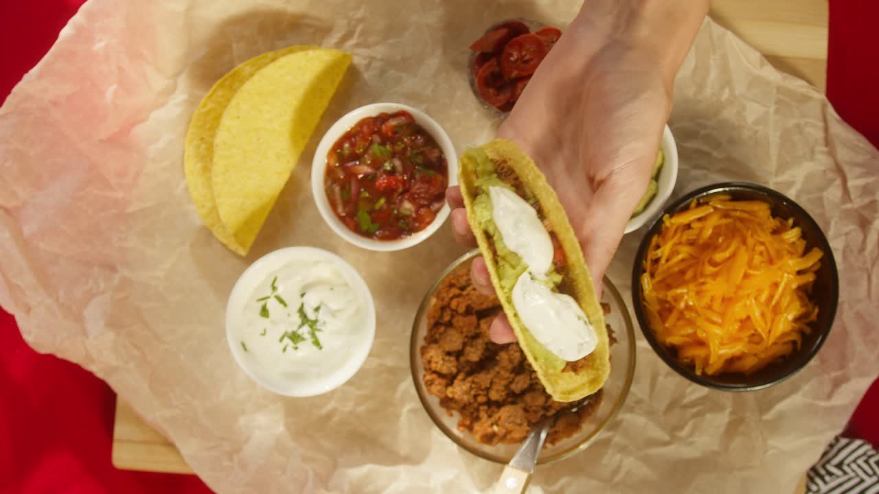 Mani che preparano un delizioso taco con guacamole, panna acida e formaggio.