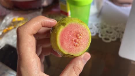 Mano-Sosteniendo-Una-Pequeña-Fruta-De-Guayaba-Tropical-Cortada-Que-Muestra-El-Rosa-Con-Semillas-Adentro-Y-El-Verde-Afuera-En-El-Estado-De-Rio-Grande-Do-Norte-En-El-Noreste-De-Brasil-En-Un-Cálido-Y-Soleado-Día-De-Verano