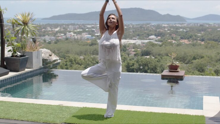 Calm woman practicing yoga poolside against beautiful landscape of sea shore