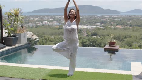 calm woman practicing yoga poolside against beautiful landscape of sea shore