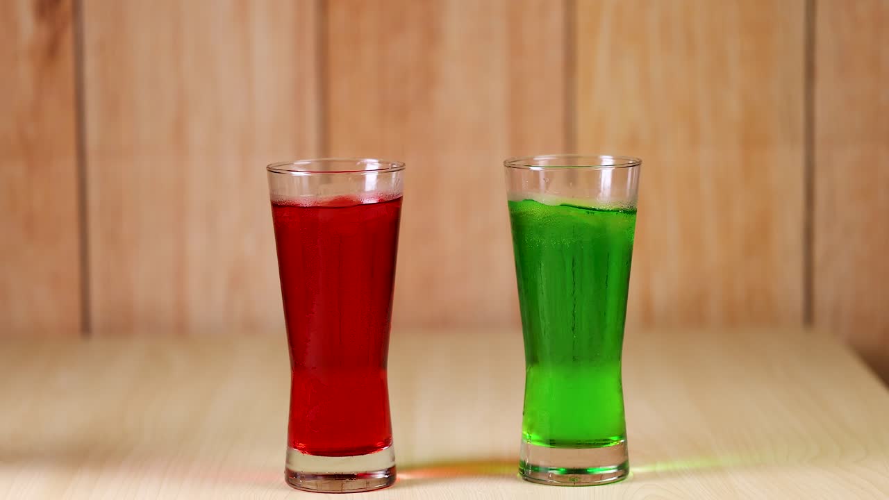 Two hands clinking red and green drinks