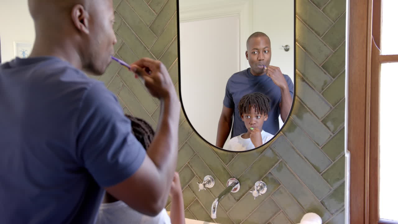 Padre e figlio afroamericani che si lavano i denti in bagno a casa, al rallentatore