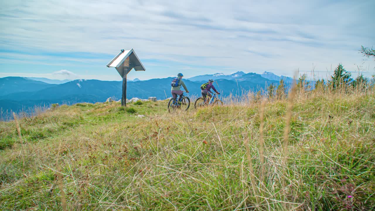 couple bikers reach the top of a hill on a mountain Alpine track. slow motion
