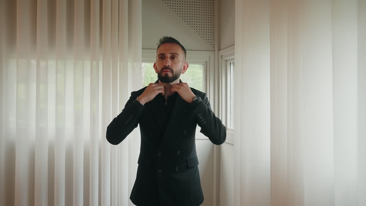 focused man in black suit buttons jacket indoors near sheer white curtains