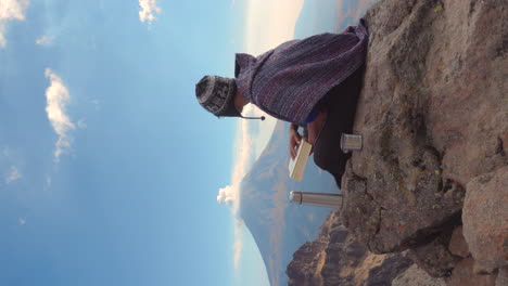 hombre sentado afuera en las rocas sosteniendo un libro y mirando el paisaje