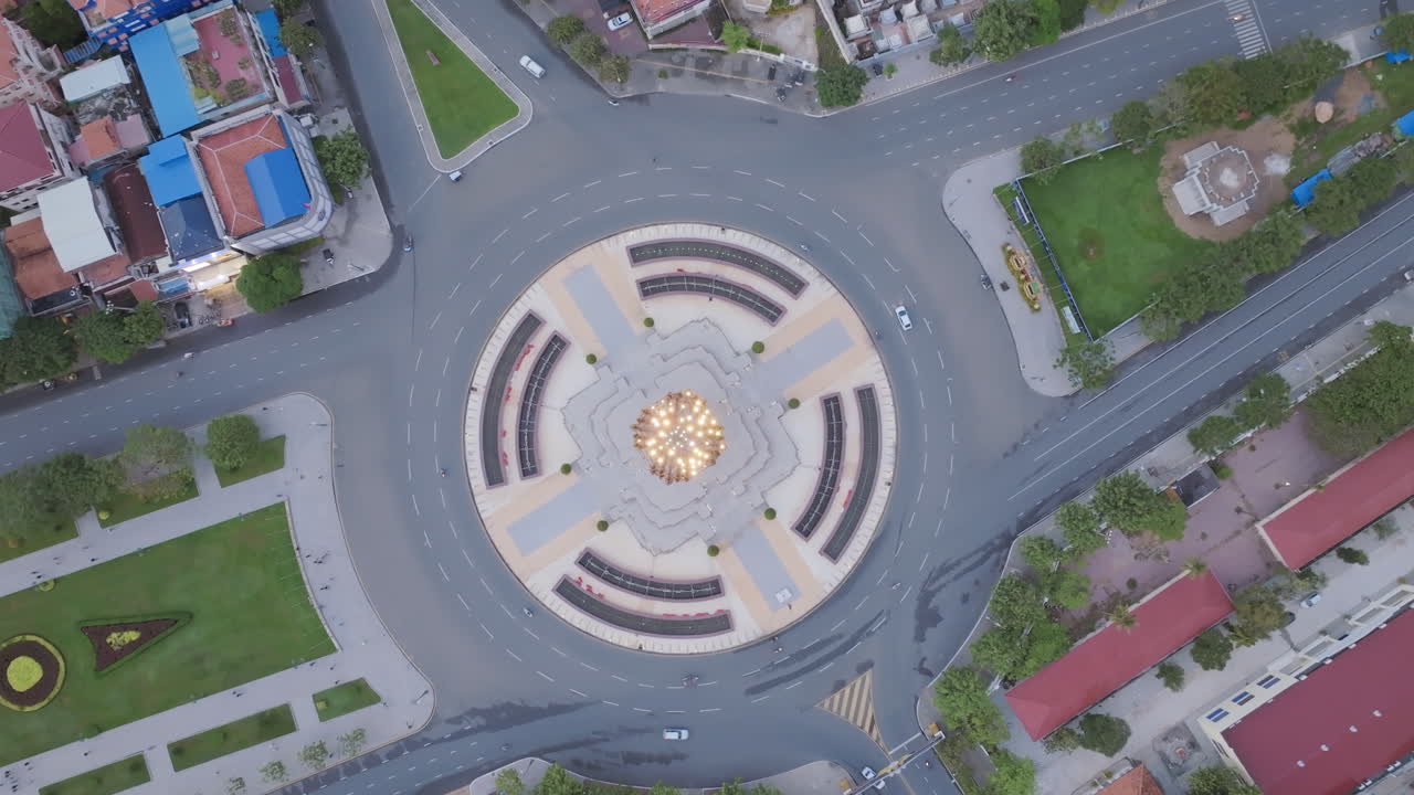 An elevated top-down perspective of the Independence Monument at twilight, surrounded by city blocks and manicured gardens, creating a radial balance of civic pride and urban growth