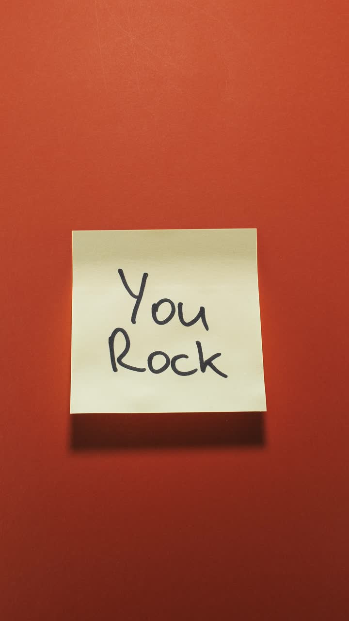 Hands posting You Rock sticky note on orange wall, conveying the idea of team praise
