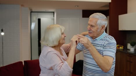 Senior-mature-couple-dancing-together-in-kitchen-at-comfortable-home-in-lockdown-for-coronavirus