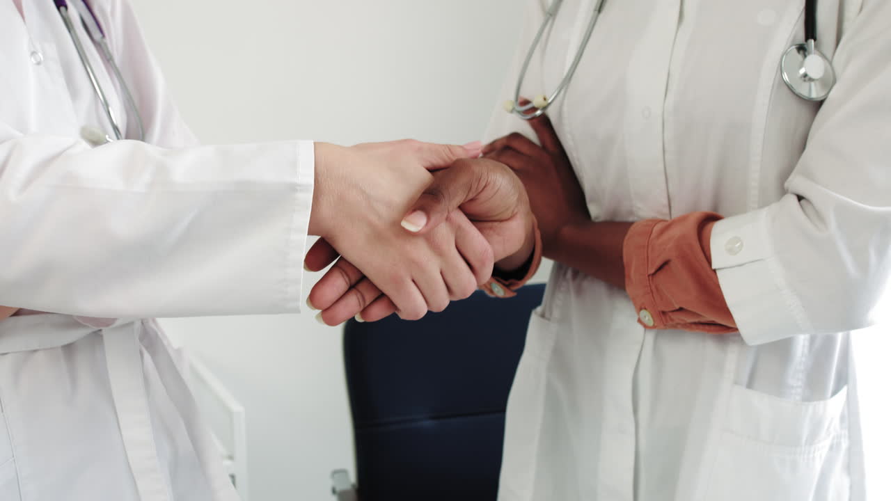 Foto ritagliata di due operatori sanitari in camice: dottori irriconoscibili che si stringono la mano in ospedale