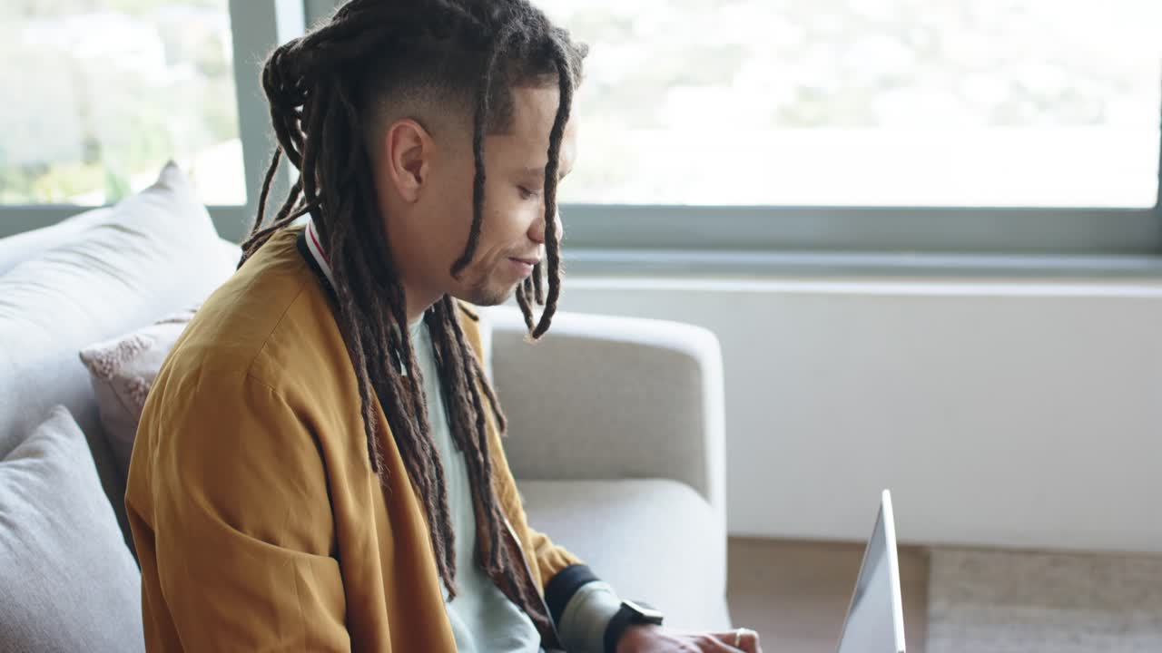 Man typing on laptop at home sofa to finish work, pausing, glancing, nodding with satisfaction