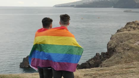 Pareja-Gay-Envuelta-En-Una-Bandera-Del-Orgullo-Mirando-Hacia-Un-Futuro-Mejor,-Homosexual-Parado-Al-Lado-De-Un-Acantilado