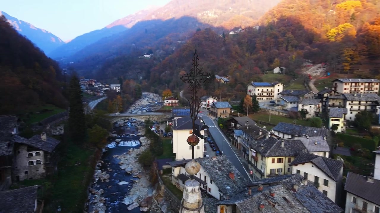 İtalya'nın Aosta Vadisi'ndeki Fontainemor Alp köyünde, Lys nehri üzerinde gün batımında bir kilisenin çan kulesi etrafında dönen drone.
