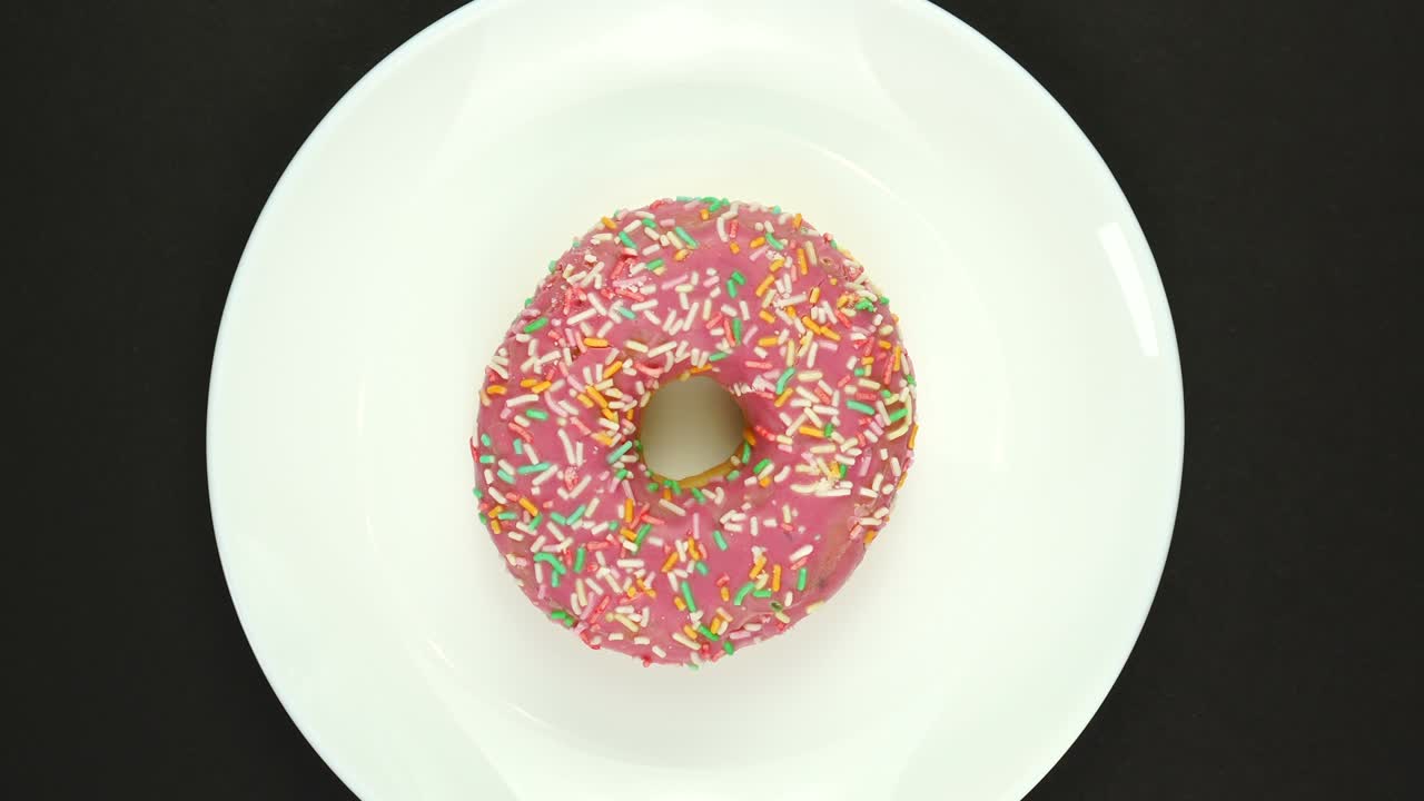 rosquilla dulce fresca girando en un plato. vista superior. rosquilla brillante y colorida disparo macro de primer plano girando sobre un fondo negro